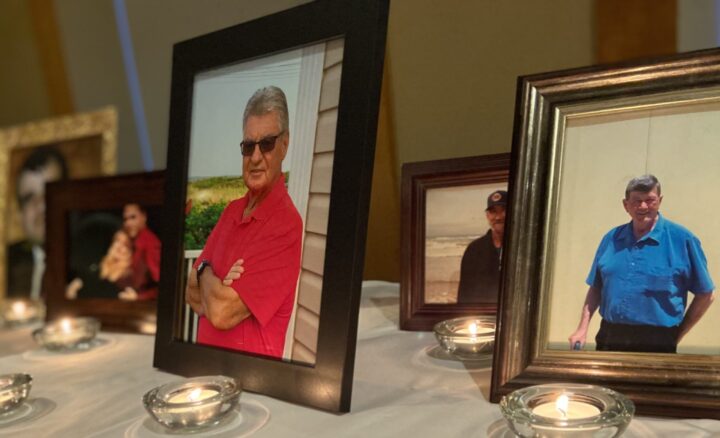 Framed photos on a white-clothed table with lit candles in front of each.