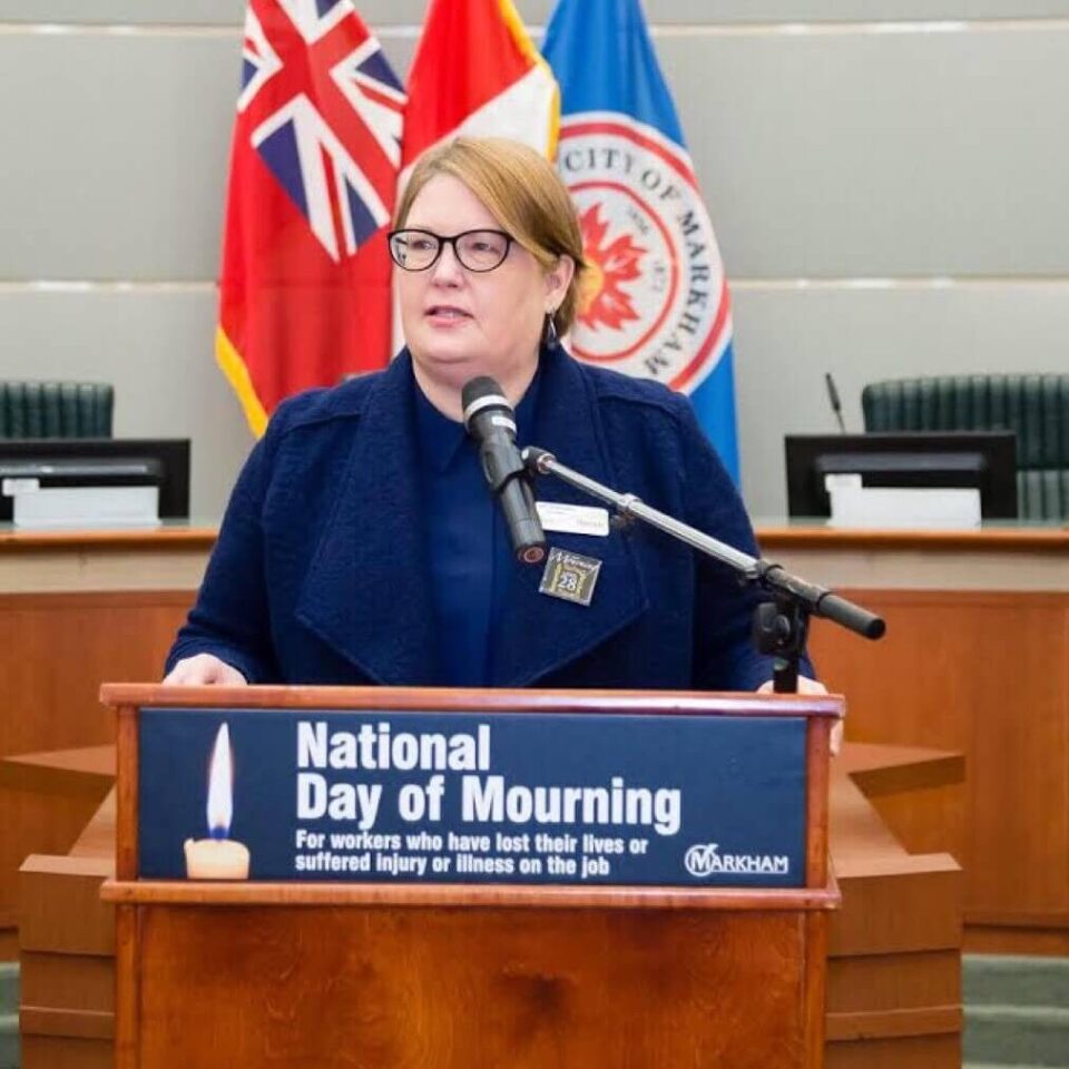 Woman at a podium speaking with Day of Mourning placard on front of podium.