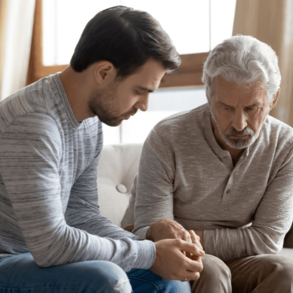 An older and younger man sit together on a couch, sharing a moment of connection and conversation.