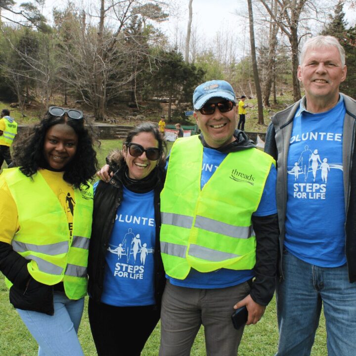 Several people gathered together in a lush green field, enjoying a sunny day outdoors. They are all wearing Threads of Life vests or T-shirts indicating they are volunteers.