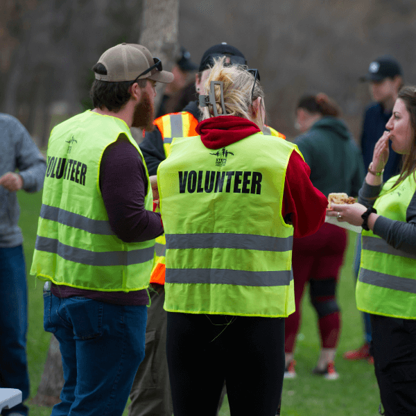 A group of people stand in a field dressed in yellow volunteer vests.