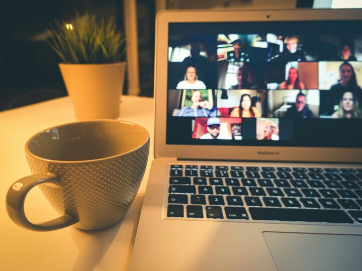 Écran d’ordinateur portable montrant une vidéoconférence à plusieurs personnes. Une tasse de café repose à côté.