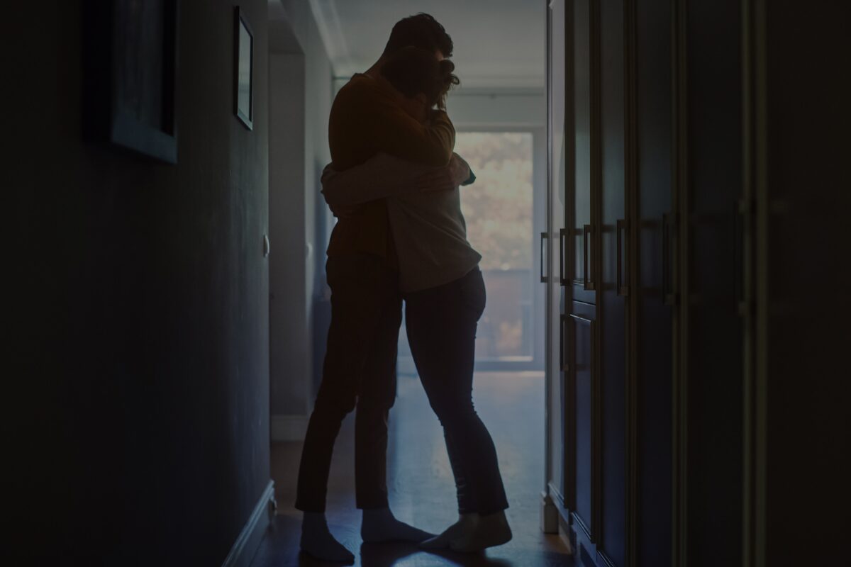 A man and woman hug in darkened hallway.