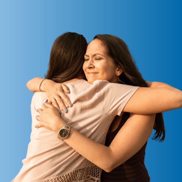 Two women hugging. We see the back of one woman's head, and the other had a relieved smile on her face.