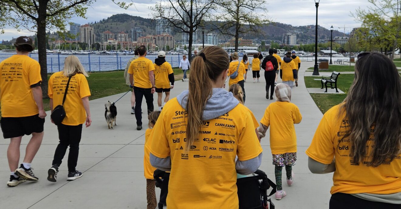 Walkers in bright yellow T-shirts walk in a crowd along the waterfront.