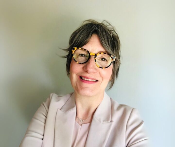 Une femme portant des lunettes à monture écaille sourit à la caméra.