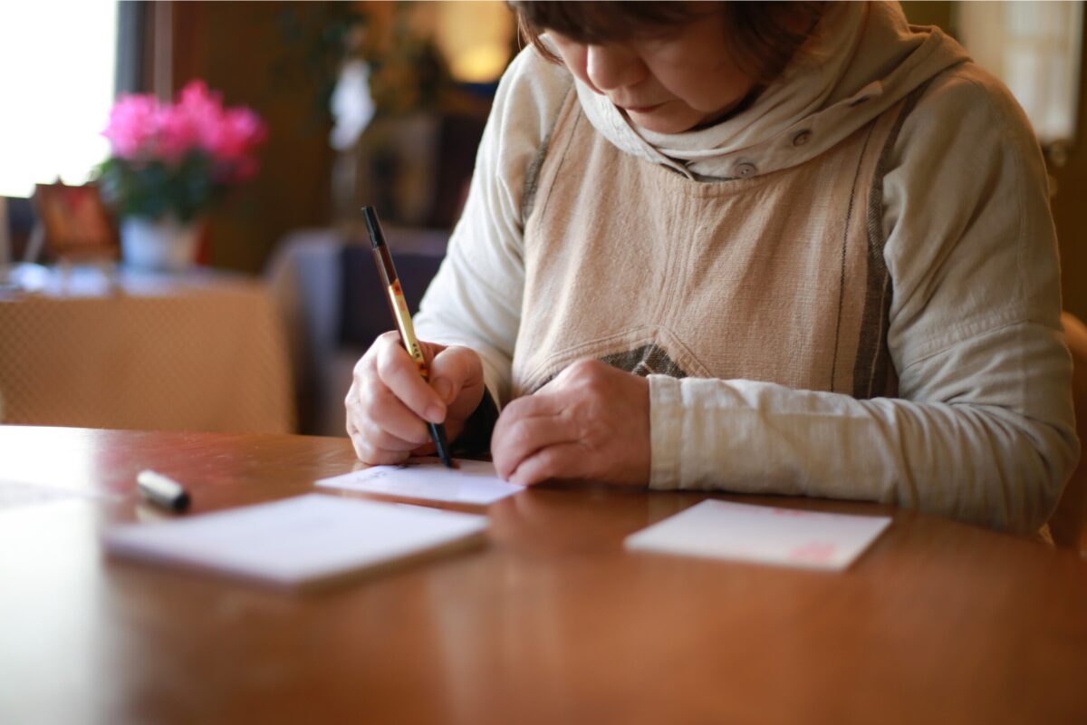A woman holding a pen as she writes a letter.
