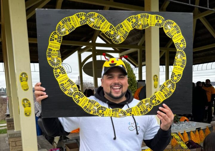 A man with a big smile stands holding a cut out Steps for Life heart around his face.