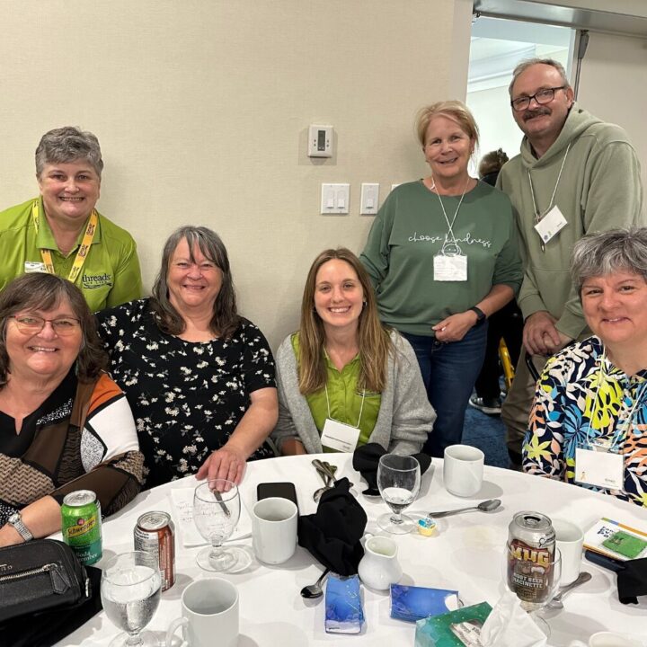 A group of people gather around a round table for a photo.