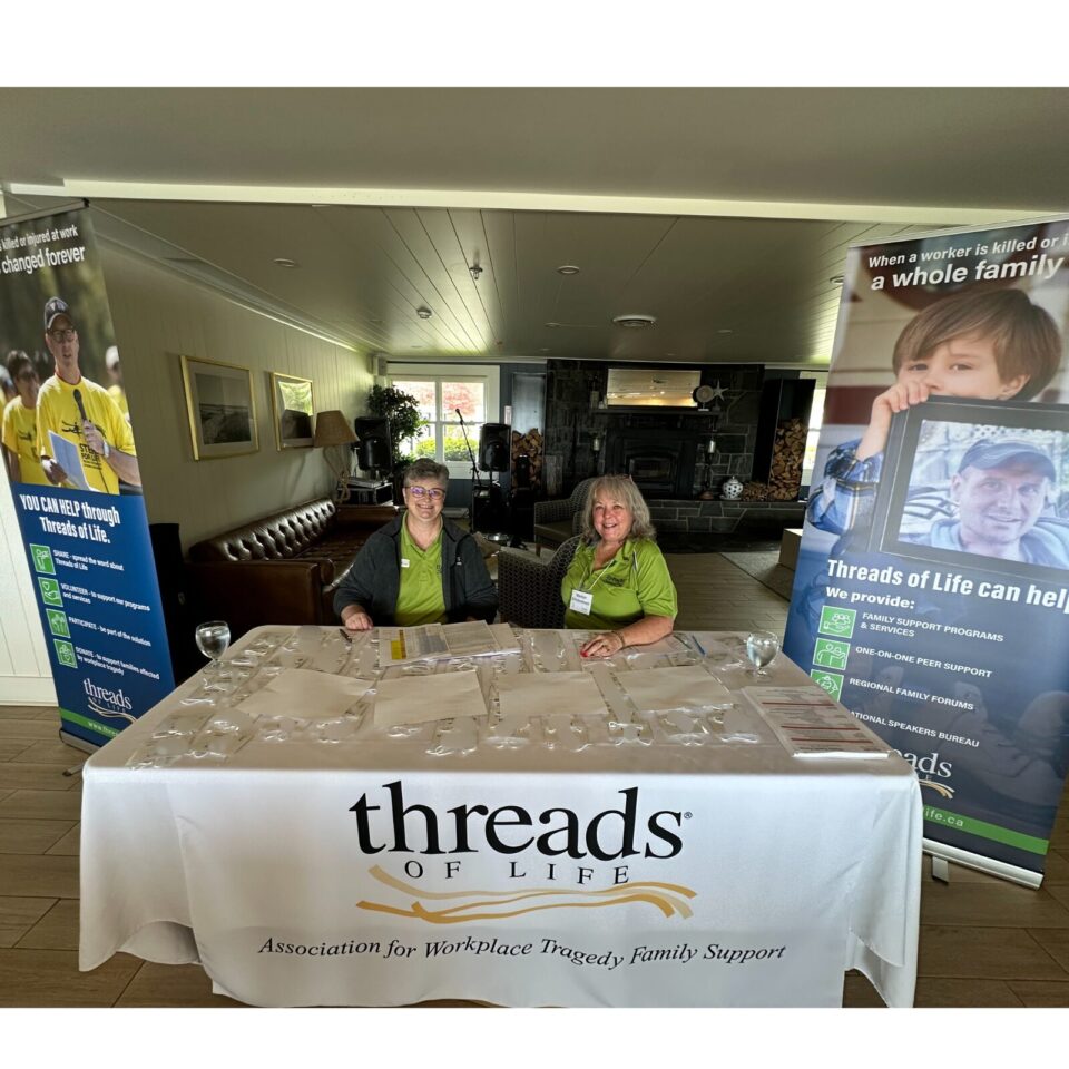 Two women sit at a table draped in a white cloth with the Threads of Life logo on it.
