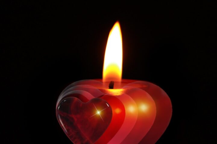 A heart-shaped candle lit in a dark room.