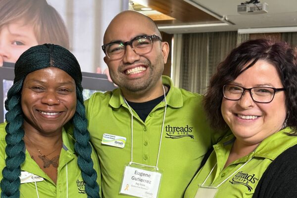 Two women and a man stand smiling. They are all wearing name badges and Threads of Liffe t-shirts.